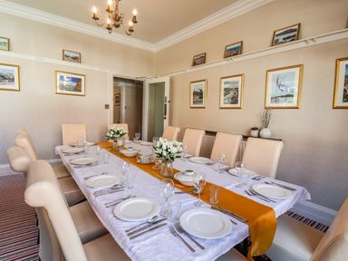 A dining room with a long table set with plates glasses and cutlery and beige chairs at Lonsdale Villa in Scarborough