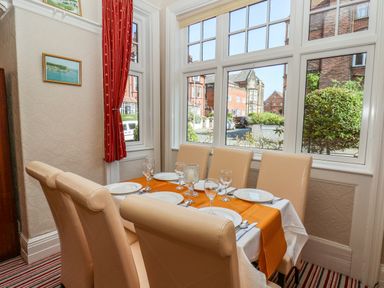 A dining area with a table set for six near large windows with red curtains at Lonsdale Villa in Scarborough