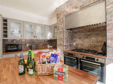 A kitchen with wooden countertops a gas stove double ovens a microwave and a basket of snacks and drinks on the counter at Lonsdale Villa in Scarborough