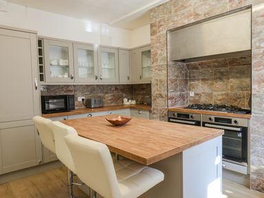 A kitchen with beige cabinets a wooden island with two white chairs and a tiled wall with a stove at Lonsdale Villa Scarborough