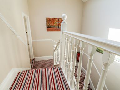 A staircase with white banisters and striped carpet with red, white, and gray lines and a fire extinguisher on the wall at Lonsdale Villa in Scarborough