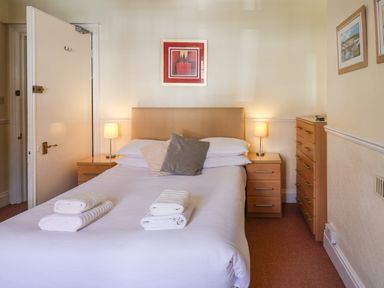A bedroom with a double bed two nightstands with lamps a chest of drawers and framed pictures on the walls at Lonsdale Villa in Scarborough