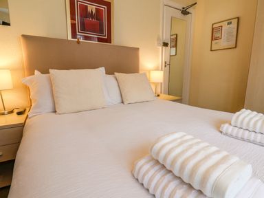 A bedroom with a bed with three pillows and folded towels on top two bedside tables with lamps and a door with a mirror at Lonsdale Villa in Scarborough