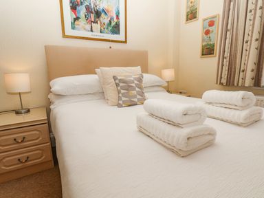 A bedroom with a bed with folded towels on it bedside tables with lamps and framed pictures on the walls at Lonsdale Villa in Scarborough