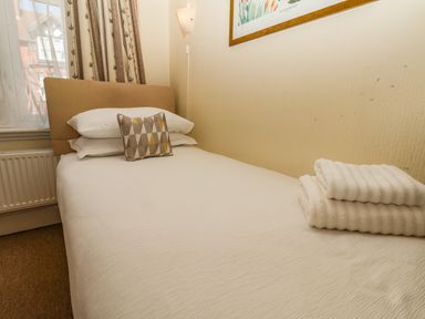 A single bed with pillows and folded towels near a window in a bedroom at Lonsdale Villa in Scarborough