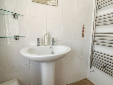 A bathroom sink with two taps a soap dispenser glass shelves and a heated towel rail at Lonsdale Villa in Scarborough