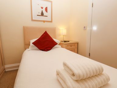 A bedroom with a single bed stack of towels on bed bedside table with lamp and framed picture on wall at Lonsdale Villa in Scarborough