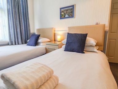 A bedroom with two single beds with blue pillows and a bedside table with a lamp at Lonsdale Villa in Scarborough