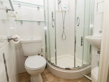 A small bathroom with a toilet a corner shower with glass doors a wall-mounted shower unit a sink and glass shelves at Lonsdale Villa in Scarborough