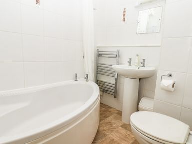 A bathroom with a bathtub a pedestal sink a toilet a towel rack and a mirror at Lonsdale Villa in Scarborough