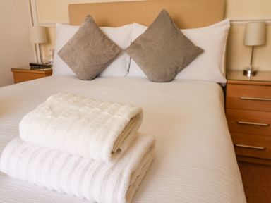 A bed with two gray pillows and folded white towels on it with bedside tables and lamps at Lonsdale Villa in Scarborough