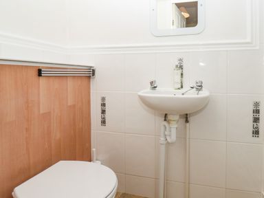 A small bathroom with a toilet wooden paneling a wall-mounted sink and a mirror above the sink at Lonsdale Villa in Scarborough