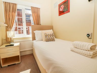 A small bedroom with a single bed bedside table lamp and window with curtains at Lonsdale Villa Scarborough