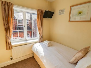 A small bedroom with a single bed folded towels a wall mounted tv and a window with curtains at Lonsdale Villa in Scarborough
