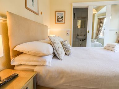 A bedroom with a bed pillows and a bedside table with a remote control and an ensuite bathroom at Lonsdale Villa in Scarborough