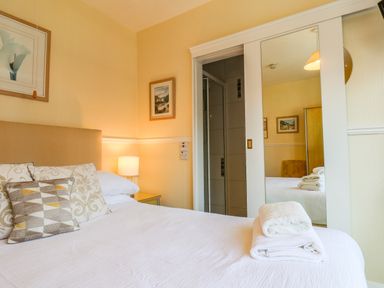 A bedroom with a bed folded towels a bedside table with lamp and a sliding door with a mirror at Lonsdale Villa in Scarborough