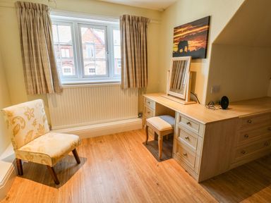 A room with a wooden floor a chair a window with curtains and a wooden desk with drawers and a mirror at Lonsdale Villa Scarborough