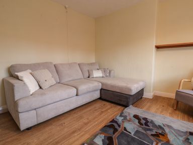A grey sectional sofa with cushions on a wooden floor next to a patterned rug and a chair in a room at Lonsdale Villa in Scarborough