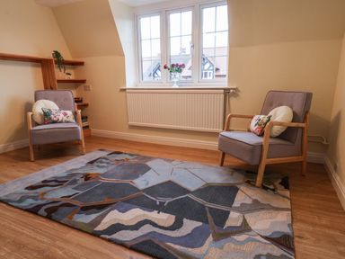 A room with two armchairs with cushions a patterned rug wooden floor and a window with a vase of flowers at Lonsdale Villa in Scarborough