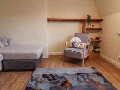 A living room with a grey armchair with cushions next to wooden corner shelves and a grey chaise lounge sofa at Lonsdale Villa in Scarborough