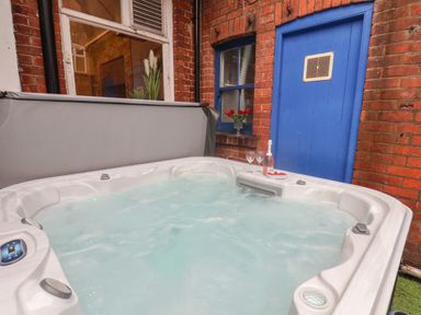 An outdoor hot tub with bubbling water next to a red brick wall with a blue door and a window with flowers at Lonsdale Villa in Scarborough