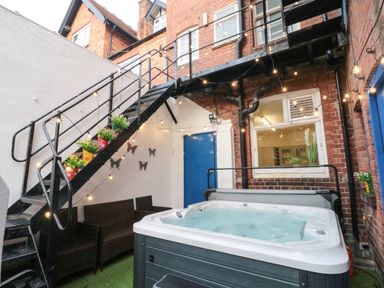 An outdoor area with a hot tub seating under stairs with potted plants and string lights at Lonsdale Villa Scarborough