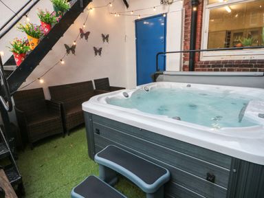 A hot tub with steps beside wicker chairs and colorful flowers on stairs at Lonsdale Villa in Scarborough