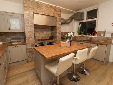 A kitchen with an island and three white stools with cabinets countertops and a window at Lonsdale Villa in Scarborough