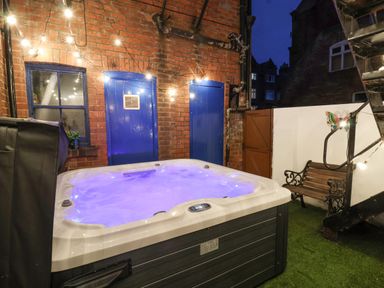 A hot tub with blue water in a backyard next to brick walls with blue doors and a wooden bench at Lonsdale Villa in Scarborough