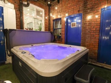 An outdoor hot tub with blue lights and string lights on a brick patio with blue doors at Lonsdale Villa in Scarborough