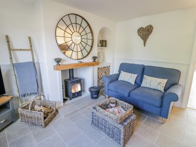 A living room with a blue sofa a wood burning stove and wicker baskets at Blossom Cottage in Broadway