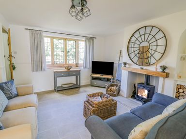 A living room with a sofa a television a fireplace with fire and a round mirror above at Blossom Cottage in Broadway