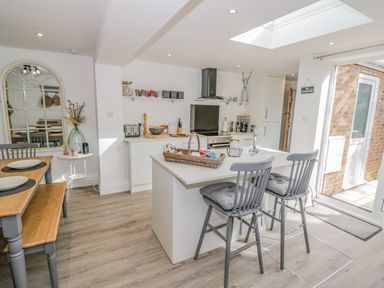 A kitchen with an island and two stools next to a dining table with bench seating at Blossom Cottage in Broadway