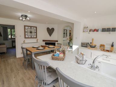 A kitchen and dining area with grey chairs a wooden table wall clock and kitchen accessories at Blossom Cottage in Broadway