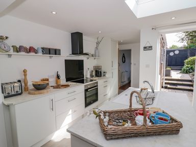 A modern kitchen with white cabinets a countertop with utensils and mugs and a door opening to a garden at Blossom Cottage in Broadway