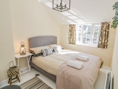 A bedroom with a bed towels window and side table with lamp at Blossom Cottage in Broadway
