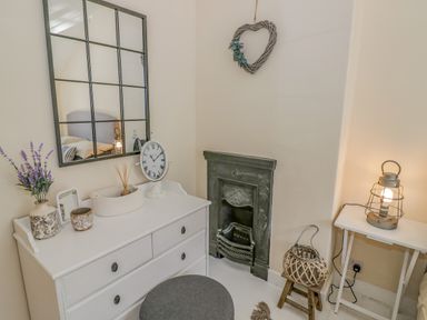 A room with a white dresser with decorative items a wall mirror a small fireplace a stool and a table with a lamp at Blossom Cottage in Broadway