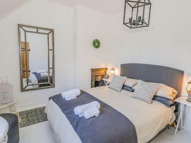A bedroom with a double bed pillows and rolled towels a large wall mirror and a small decorative fireplace at Blossom Cottage in Broadway