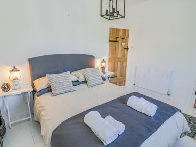 A bedroom with a double bed, two rolled towels on the bed, bedside tables with lamps, and a wooden door at Blossom Cottage in Broadway