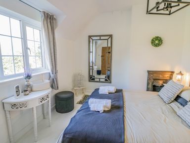 A bedroom with a bed having folded towels a mirror white table with flowers and a window at Blossom Cottage in Broadway