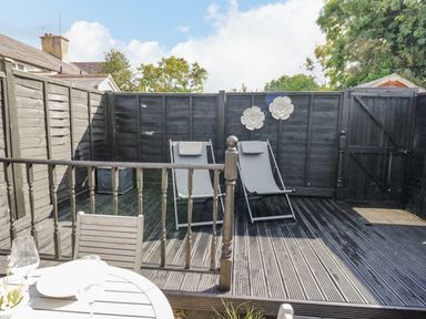 An outdoor patio with two lounge chairs wooden fencing and a small table with chairs at Blossom Cottage in Broadway
