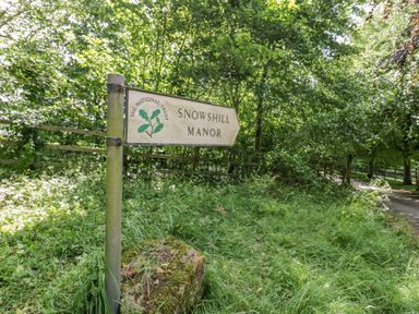 A signpost for Snowshill Manor surrounded by grass trees and a wooden fence at Blossom Cottage in Broadway