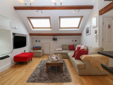 A living room with a beige sofa with red cushions a wooden coffee table on a rug and skylights at Apartment 2 Gorwel Glas in Llanbedrog