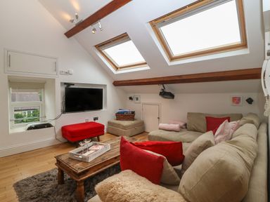 A living room with a beige sectional sofa red cushions wooden coffee table mounted TV and skylight windows at Apartment 2 Gorwel Glas in Llanbedrog
