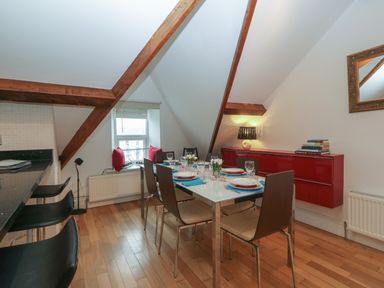 A dining area with a set table and six chairs under a slanted ceiling with exposed wooden beams at Apartment 2 Gorwel Glas in Llanbedrog