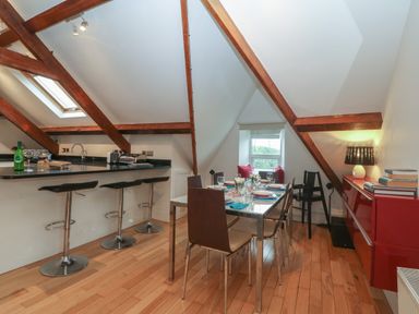 A dining area with table and chairs next to a kitchen counter with stools under exposed wooden beams at Apartment 2 Gorwel Glas in Llanbedrog