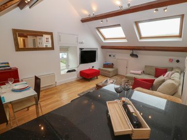 A living room with a beige sofa red cushions skylights a TV on the wall and a dining table with plates at Apartment 2 Gorwel Glas Llanbedrog