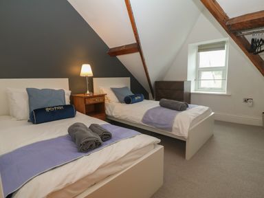 A bedroom with two single beds a bedside table with a lamp a small chest of drawers and a window at Apartment 2 Gorwel Glas in Llanbedrog