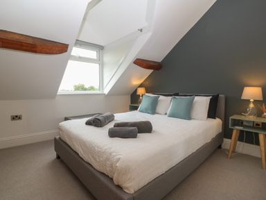A bedroom with a double bed with white bedding and folded towels on it bedside tables with lamps and pillows at Apartment 2 Gorwel Glas Llanbedrog