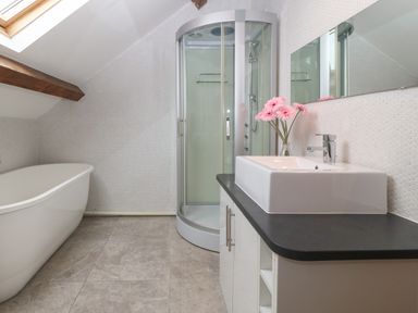 A bathroom with a white bathtub a corner shower a sink with a black countertop and pink flowers in Llanbedrog